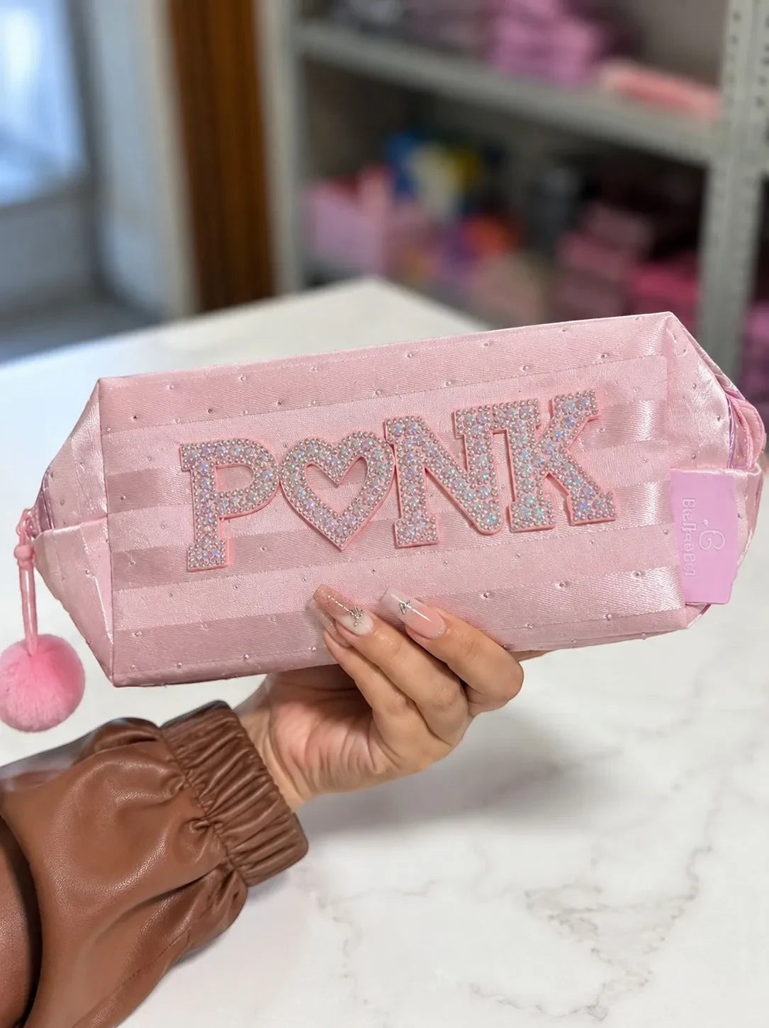 Neceser ÉL&ELLA MAKEUP Y ACCESORIOS rosa satinado con letras brillantes PINK y pompón decorativo en mano